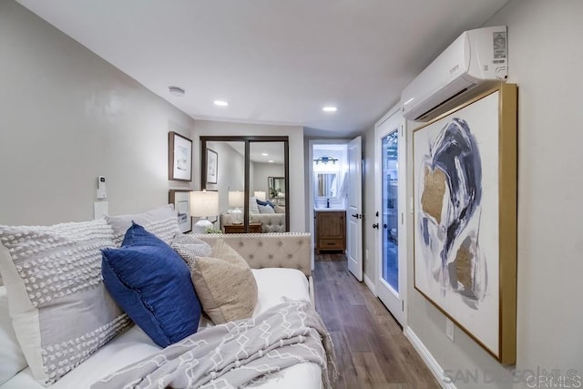 bedroom with ensuite bathroom, a wall mounted AC, and dark hardwood / wood-style floors