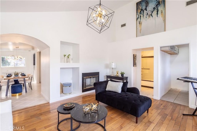 living room with a high ceiling, wood-type flooring, built in shelves, and a chandelier