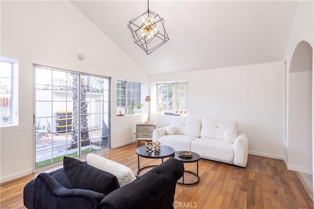 living room with light wood-type flooring, a healthy amount of sunlight, high vaulted ceiling, and a notable chandelier