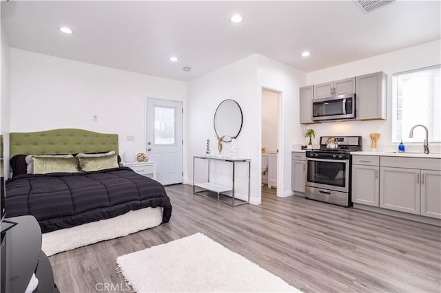 bedroom with connected bathroom, light hardwood / wood-style flooring, and sink