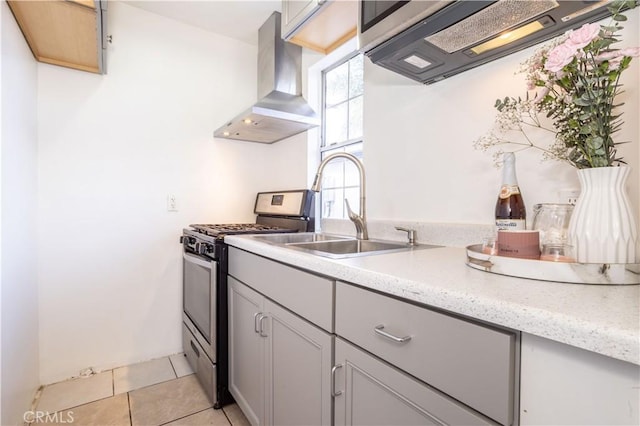 kitchen featuring sink, light tile patterned flooring, stainless steel gas range, gray cabinetry, and wall chimney exhaust hood