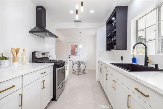 kitchen with white cabinets, stainless steel gas range, decorative light fixtures, wall chimney range hood, and sink