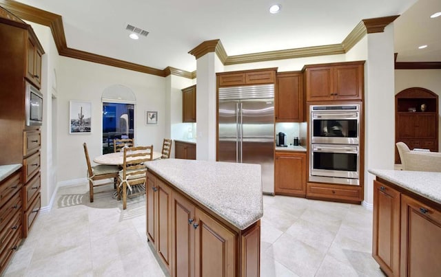 kitchen featuring built in appliances, crown molding, a kitchen island, and light tile patterned floors