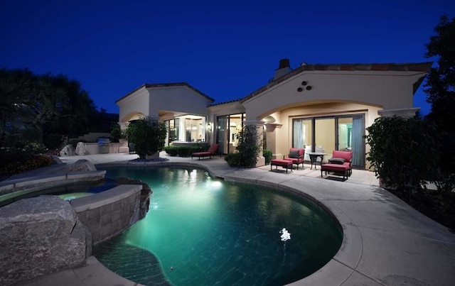 pool at night featuring an in ground hot tub and a patio