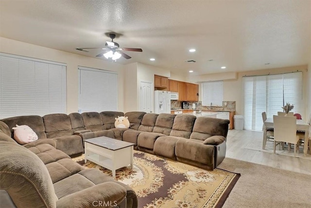 living room featuring a textured ceiling, ceiling fan, light wood-type flooring, and sink