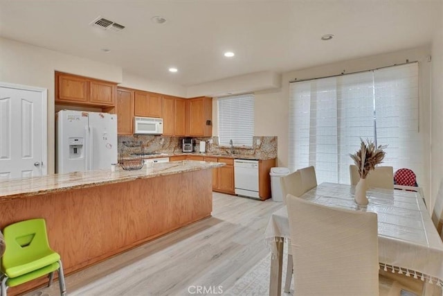 kitchen featuring light hardwood / wood-style floors, light stone countertops, white appliances, and tasteful backsplash