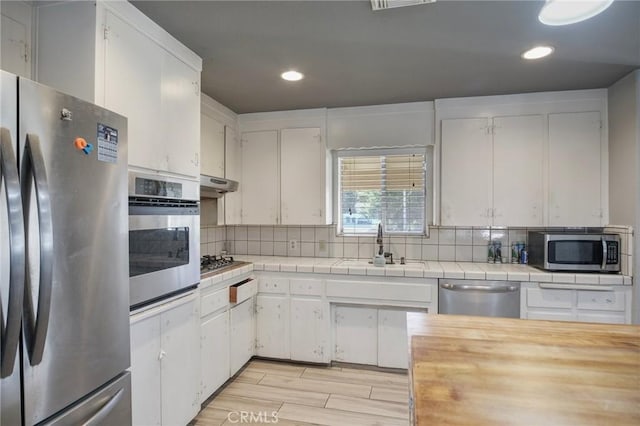 kitchen featuring stainless steel appliances, backsplash, white cabinetry, and tile counters