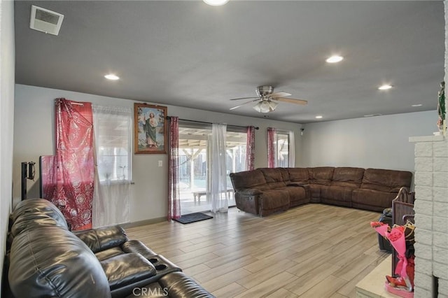 living room with a brick fireplace, ceiling fan, and light wood-type flooring