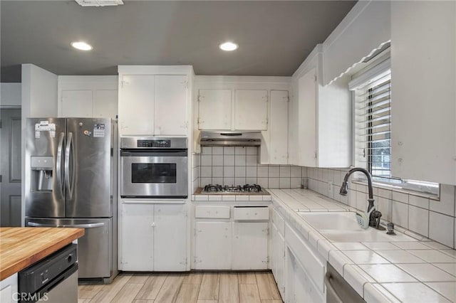 kitchen with stainless steel appliances, decorative backsplash, tile counters, white cabinets, and sink