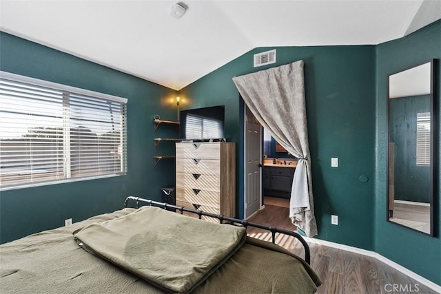 bedroom with hardwood / wood-style floors, lofted ceiling, and ensuite bath