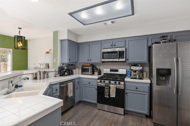 kitchen featuring stainless steel appliances, tile counters, dark hardwood / wood-style flooring, pendant lighting, and sink