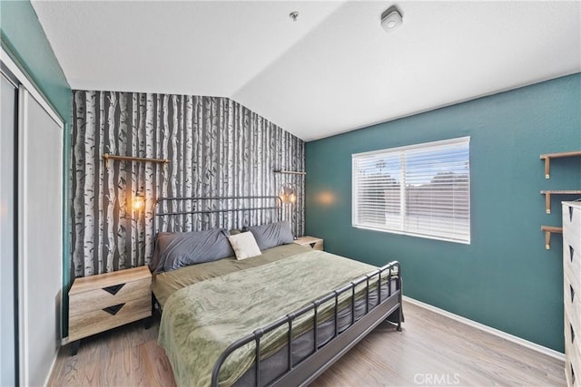 bedroom with light hardwood / wood-style floors, lofted ceiling, and a closet