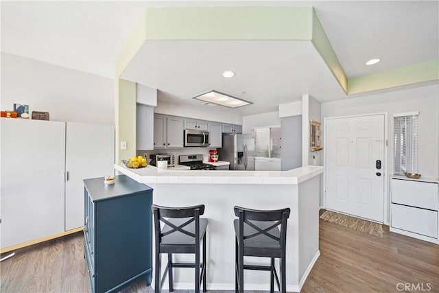 kitchen with appliances with stainless steel finishes, dark wood-type flooring, gray cabinets, a kitchen bar, and kitchen peninsula