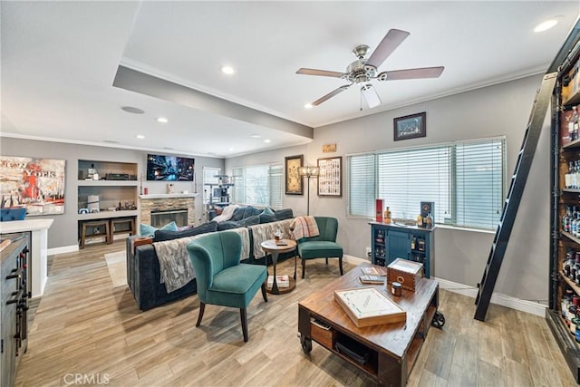 living room with a fireplace, built in features, ceiling fan, light hardwood / wood-style flooring, and crown molding