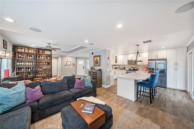 living room with light hardwood / wood-style floors, ceiling fan, ornamental molding, and wet bar