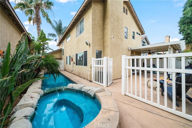 back of property featuring ceiling fan, a swimming pool with hot tub, and a patio