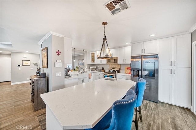 kitchen featuring light hardwood / wood-style flooring, decorative light fixtures, white cabinetry, stainless steel appliances, and a center island with sink