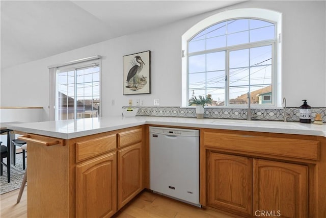 kitchen with sink, dishwasher, tasteful backsplash, kitchen peninsula, and light wood-type flooring