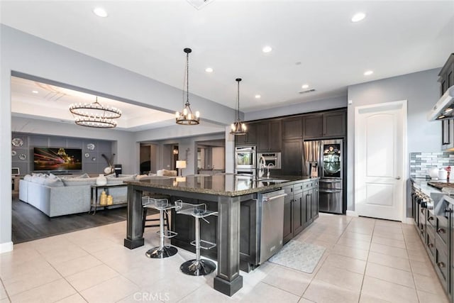 kitchen with appliances with stainless steel finishes, a kitchen breakfast bar, backsplash, a kitchen island with sink, and dark brown cabinets