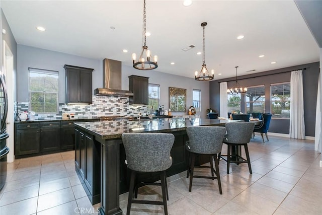 kitchen featuring decorative light fixtures, wall chimney range hood, an inviting chandelier, dark stone countertops, and a large island