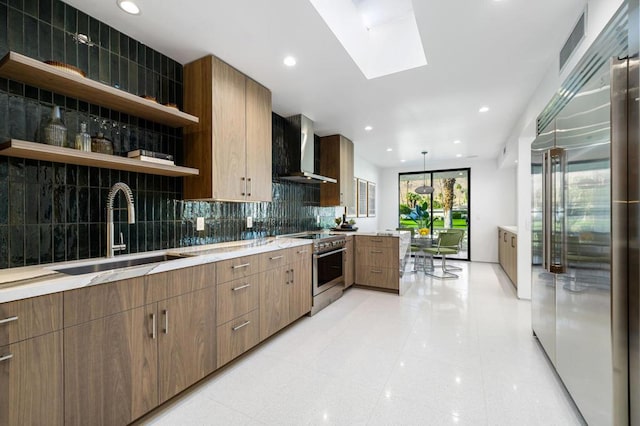 kitchen with tasteful backsplash, sink, a skylight, appliances with stainless steel finishes, and wall chimney exhaust hood