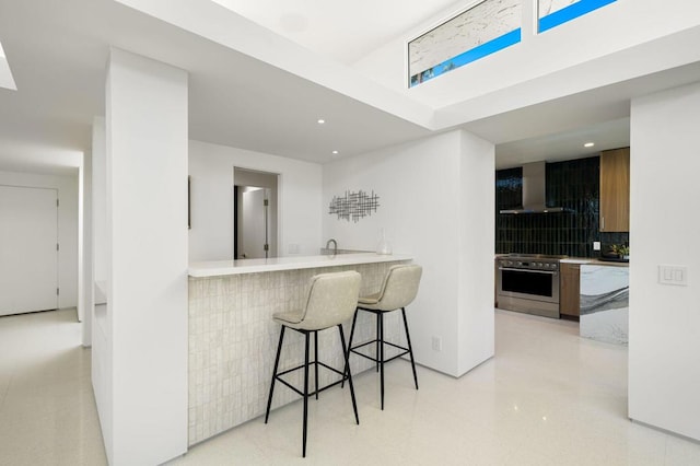 kitchen featuring high end range, kitchen peninsula, decorative backsplash, a breakfast bar area, and wall chimney exhaust hood