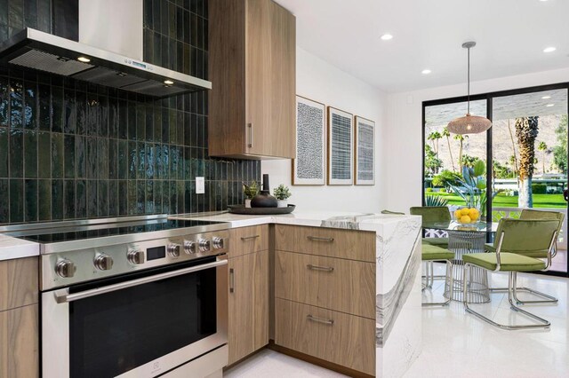 kitchen featuring high end stainless steel range oven, backsplash, wall chimney exhaust hood, and hanging light fixtures