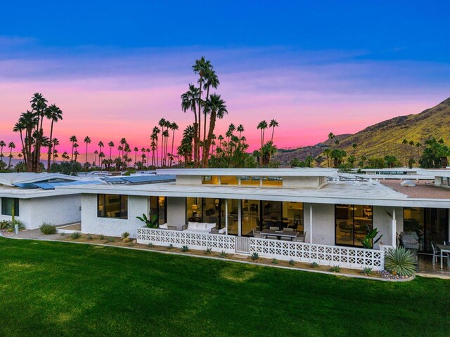 back house at dusk featuring a mountain view and a lawn