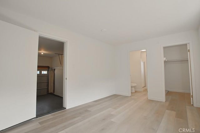 unfurnished bedroom featuring ensuite bath, a walk in closet, a closet, and light hardwood / wood-style flooring