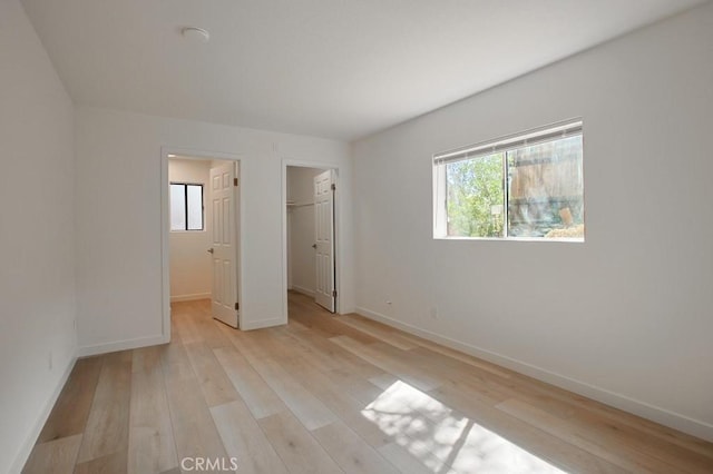 unfurnished bedroom featuring light wood-type flooring, a walk in closet, and a closet