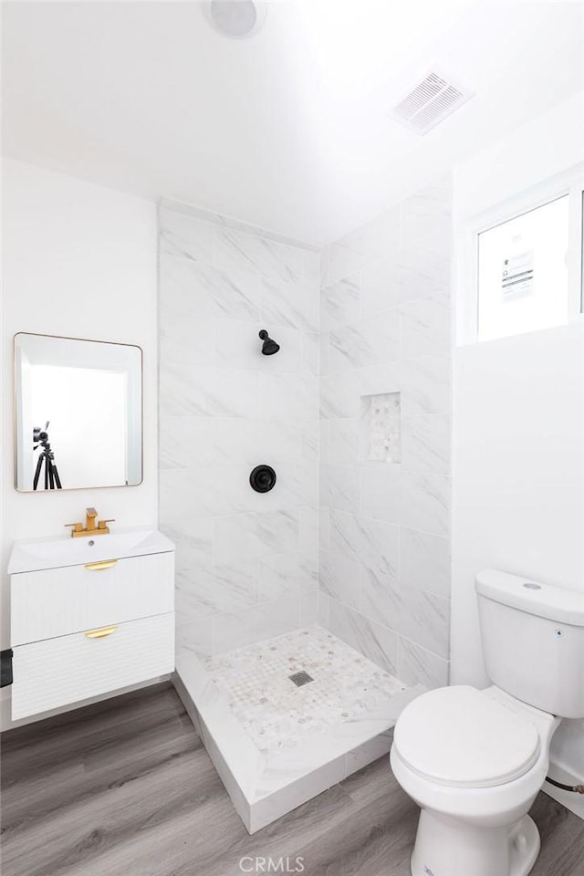 bathroom with wood-type flooring, tiled shower, vanity, and toilet