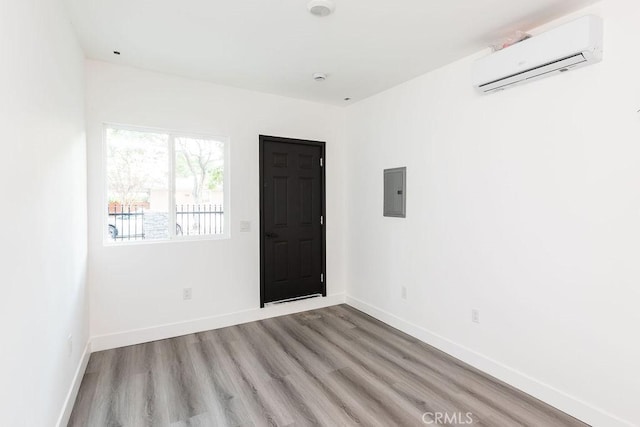 empty room with electric panel, light hardwood / wood-style floors, and a wall unit AC