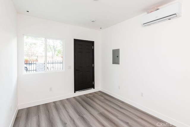 empty room featuring light hardwood / wood-style floors, electric panel, and a wall unit AC