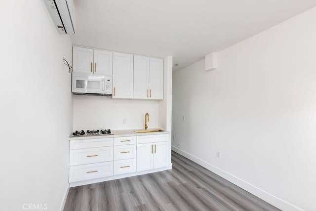 kitchen with stainless steel gas stovetop, white cabinetry, a wall unit AC, light hardwood / wood-style flooring, and sink