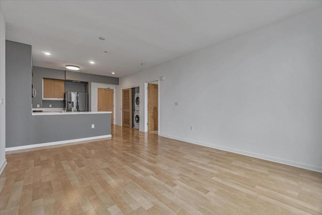 unfurnished living room featuring light hardwood / wood-style flooring and stacked washer and clothes dryer