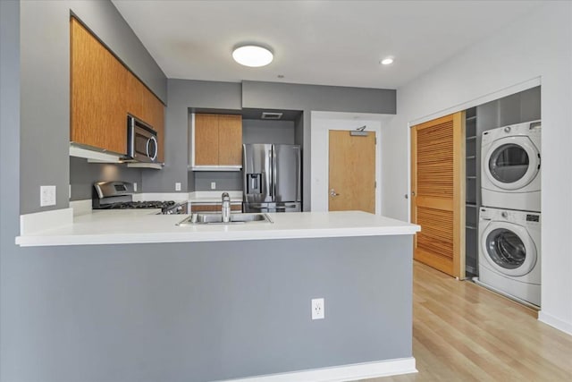 kitchen with sink, stacked washer and clothes dryer, kitchen peninsula, and appliances with stainless steel finishes