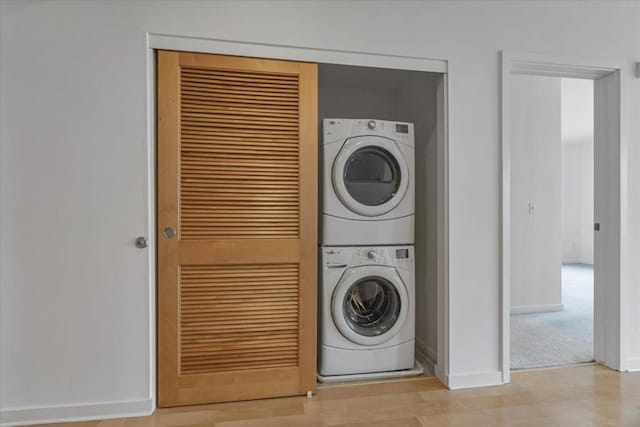 laundry area with stacked washer / drying machine and light wood-type flooring