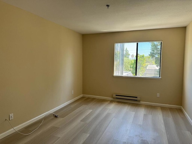 unfurnished room with a baseboard heating unit and light hardwood / wood-style floors