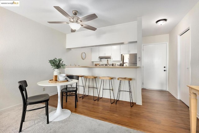 kitchen featuring ceiling fan, dark hardwood / wood-style floors, kitchen peninsula, white cabinetry, and stainless steel fridge