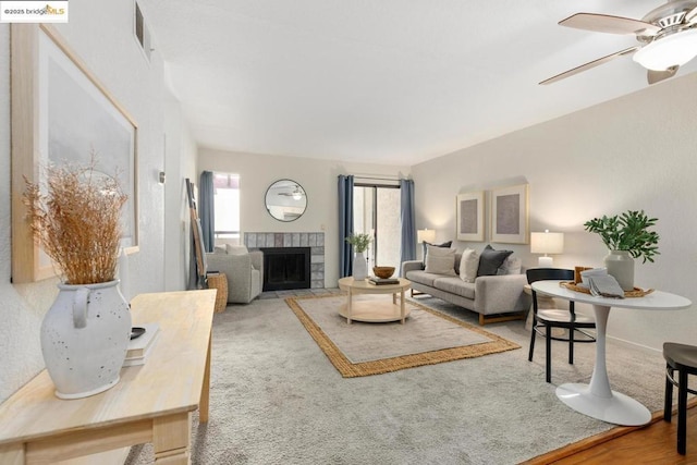 living room featuring ceiling fan, carpet, and a tile fireplace