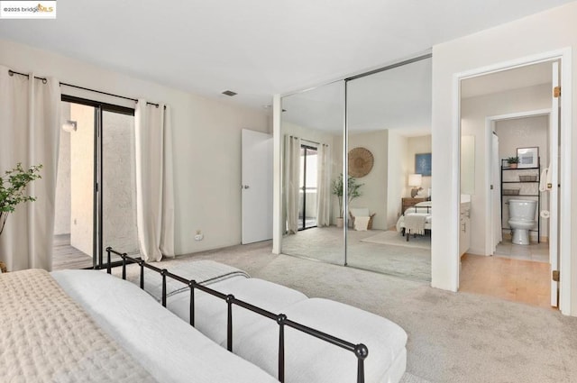 bedroom featuring light colored carpet, a closet, and ensuite bath