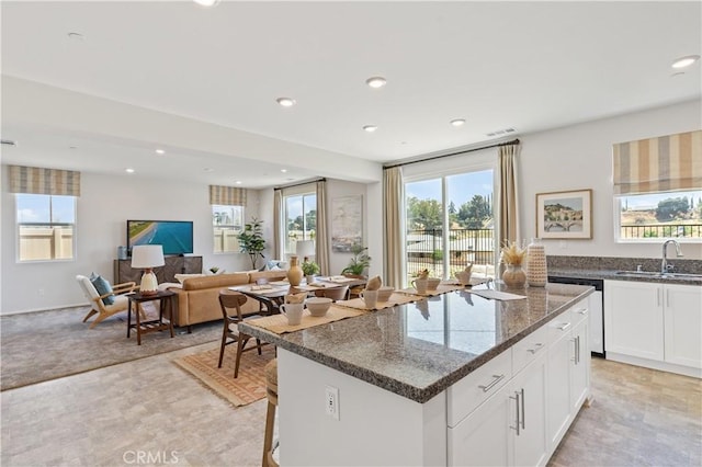 kitchen with white cabinetry, sink, dark stone countertops, stainless steel dishwasher, and a center island