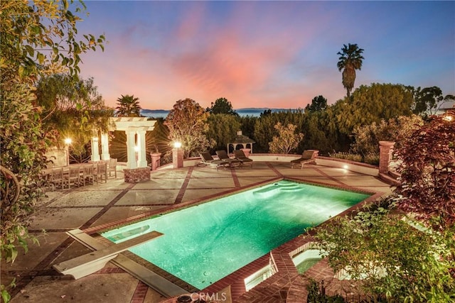 pool at dusk with a diving board, an in ground hot tub, and a patio