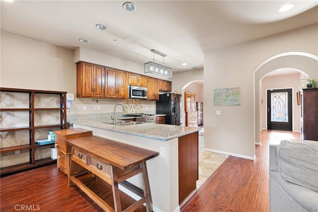 kitchen with sink, hanging light fixtures, black fridge, kitchen peninsula, and light stone counters