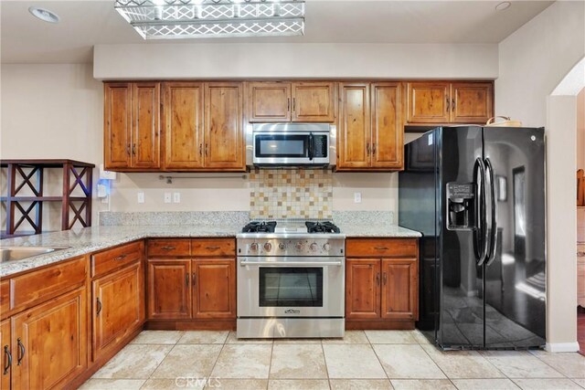 kitchen featuring light tile patterned floors, decorative backsplash, light stone counters, and stainless steel appliances