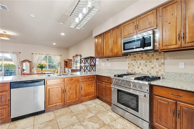 kitchen with light stone countertops, appliances with stainless steel finishes, sink, backsplash, and kitchen peninsula