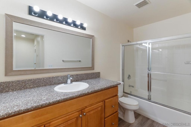 full bathroom with toilet, enclosed tub / shower combo, hardwood / wood-style floors, and vanity