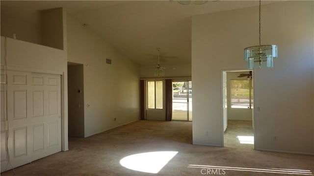 empty room with light colored carpet, ceiling fan with notable chandelier, and high vaulted ceiling