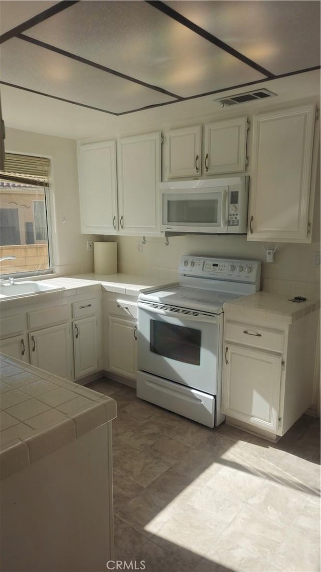 kitchen featuring tile countertops, sink, white cabinetry, and white appliances