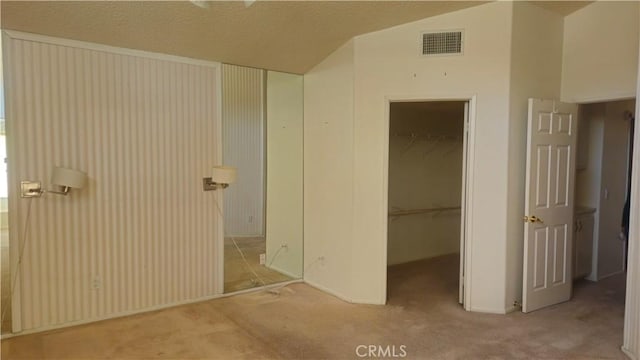 unfurnished bedroom with carpet floors, a walk in closet, a closet, and vaulted ceiling